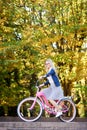 Blond long-haired attractive girl on pink lady bicycle in sunny autumn park on trees background. Royalty Free Stock Photo