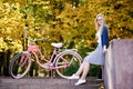 Blond long-haired attractive girl on pink lady bicycle in sunny autumn park on trees background. Royalty Free Stock Photo