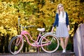 Blond long-haired attractive girl on pink lady bicycle in sunny autumn park on trees background. Royalty Free Stock Photo