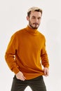 blond man in an orange sweater on a light background and dark trousers cropped view Royalty Free Stock Photo