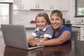 Blond mother woman together with her young beautiful and sweet little girl 6 to 8 years old sitting at home kitchen enjoying with Royalty Free Stock Photo