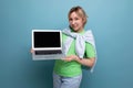 blond positive attractive girl in casual outfit shows screen with mockup on laptop on blue background