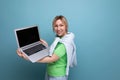 blond positive attractive girl in casual outfit shows screen with mockup on laptop on blue background