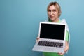 blond positive cute female freelancer in casual outfit showing screen with mockup on laptop on blue background