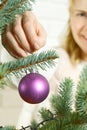 Blond pretty woman decorating christmas tree with purple ornaments decor balls. Royalty Free Stock Photo