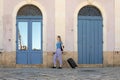 Blond satisfied and free woman walking with luggage in between two doors. Moving on, travel destination, summer vacation