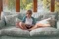 Blond school boy sitting on sofa, having fun at home, using smartphone and laughing, playing video game on mobile phone Royalty Free Stock Photo