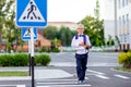 A blond schoolboy with glasses and a backpack goes to school on a pedestrian crosswalk. Day of knowledge