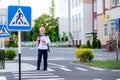 A blond schoolboy with glasses and a backpack goes to school on a pedestrian crosswalk. Day of knowledge