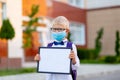 A blond schoolboy with glasses and a protective mask stands at the school and holds a sign with a white sheet. Day of knowledge.