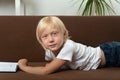Blond schoolboy is lying on couch with book. Portrait of boy with textbook