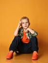 Blond schoolboy, regular guy in checkered shirt, orange t-shirt, jeans sits on floor. Gesturing. Holding finger up Royalty Free Stock Photo