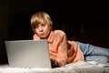 Blond serious boy spending time with notebook, lying on the floor Royalty Free Stock Photo