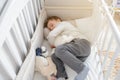 Blond seven years boy sleeping in his sister white wooden cot in white shirt and grey trousers with toys in his arms