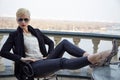Blond short haircut woman sexy skinny clothes jacker lather pants sunglasses beautiful view river balcony date meeting successful Royalty Free Stock Photo