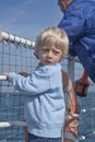 Blond Small child clinging to the railing on ferry, looking back for taking a look, in the background a beautiful blue sea