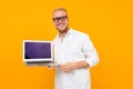 Blond smart smiling businessman in white shirt with laptop with mockup on yellow background