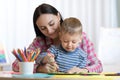 Blond smiling little boy hold in hand pencil drawing something together with mom.