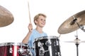 Blond teen boy plays drums at drumkit in studio against white ba Royalty Free Stock Photo