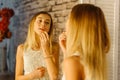 The blond teenager is applying the lips. The close-up reflection in the mirror.