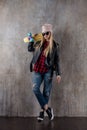 Blond teenager girl in black sunglasses and pink hat with blue skateboard. In front of concrete wall. Royalty Free Stock Photo