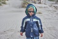 Blond toddler in blue windbreaker, looking cool with sunglasses, at a northern beach in Denmark with dry plants in the background Royalty Free Stock Photo