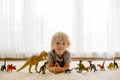 Blond toddler child, playing with dinosaurs at home