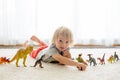 Blond toddler child, playing with dinosaurs at home