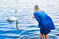 Blond woman in blue dress feeding a swan at lake