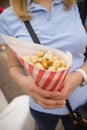 Blond woman in a blue t-shirt with striped paper bag full of popcorn. Girl holding and eating sweet popcorn Royalty Free Stock Photo