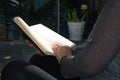 Blond woman with curly hair reading a book by the window