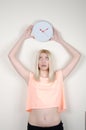 Blond woman with green eyes leaning on white wall, holding a wall clock Royalty Free Stock Photo