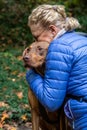 Blond woman hugging two toned brown Doberman mix rescue dog, outside in nature