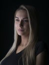 Blond woman with long hair and bright eyes wearing black t-shirt, closeup studio portrait on dark background Royalty Free Stock Photo