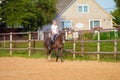 Blond woman with long hair jockey rider on a bay horse, in a paddock on a ranch Royalty Free Stock Photo