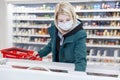 A blond woman in a medical mask takes out frozen food from a refrigerator in a supermarket. Precautions during the coronavirus