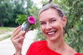 Blond woman outdoors holding a miniature watering can with a flower