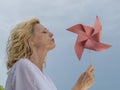 A blonde woman plays with a red pinwheel by blowing to make it spin Royalty Free Stock Photo