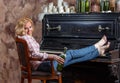 Blond woman posing near retro piano with waxed wine bottle