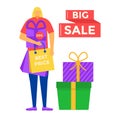 Blond woman shopping, holding bags and standing next to gift boxes with big sale sign. Consumer at a seasonal sale with Royalty Free Stock Photo