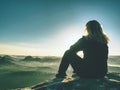 Blond woman sitting on edge of the mountain cliff against surise