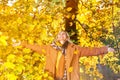 Blond woman standing beneath a tree and enjoying the autumn weather