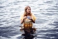 Woman in yellow historic dress standing in the water holding a teacup