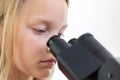 A blond 9 year old schoolchild looks into the eyepiece of a microscope. Isolated