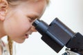 A blond 7 year old schoolchild looks into the eyepiece of a microscope. Isolated