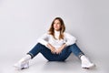 Blonde adolescent in jeans, sweater, socks and sneakers. Smiling, sitting on floor, legs wide apart, isolated on white. Close up Royalty Free Stock Photo