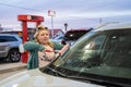 Blonde adult woman washes the windshield with a Squeegee while filling up the car with gas at a gas