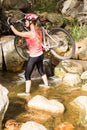 Blonde athlete carrying her mountain bike over stream Royalty Free Stock Photo