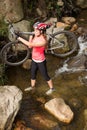 Blonde athlete carrying her mountain bike over stream Royalty Free Stock Photo