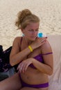 A blonde on the beach applies a cream on her shoulder.